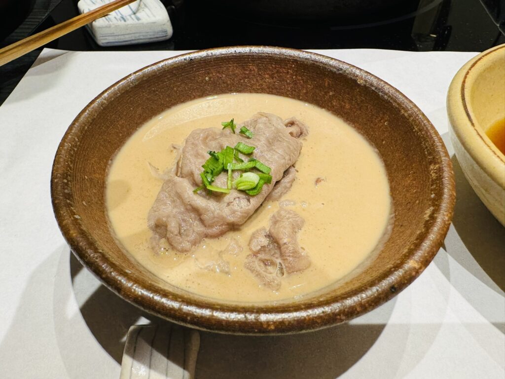 ごまだれの器で、しゃぶしゃぶした和牛を薬味のねぎと一緒に