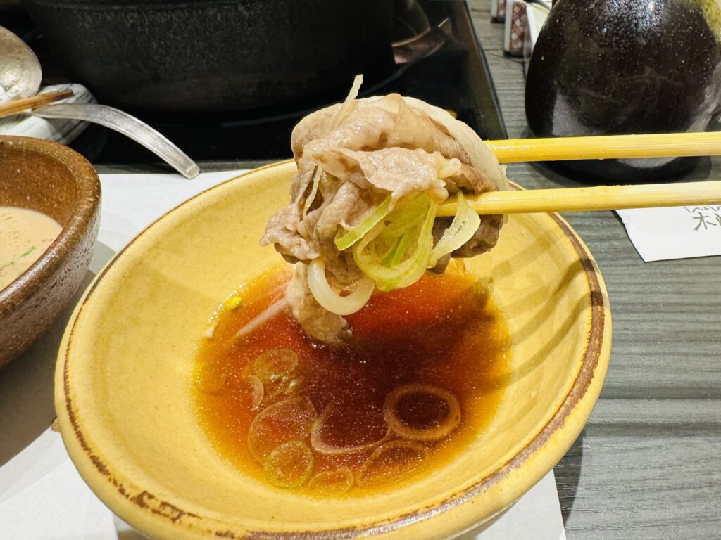 ぽん酢の器で、葱を添えたしゃぶしゃぶ肉を箸で持ち上げた一枚