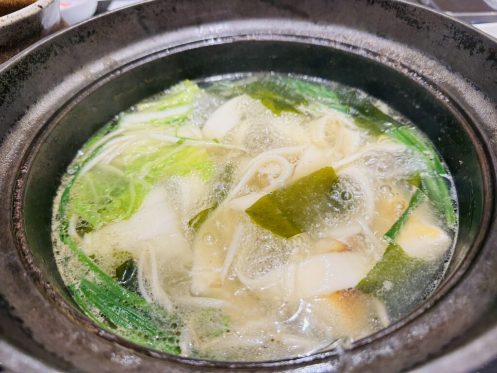 鍋だしで煮えているきしめんと餅、昆布、青菜のアップ