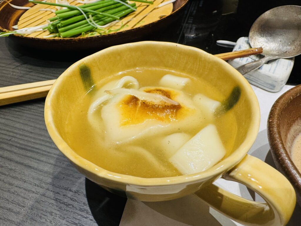 だしスープに入ったきしめんと餅を黄色い器で取り分けたところ