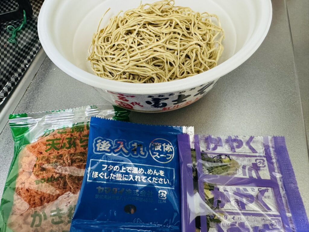 カップの中の乾麺と、取り出した小袋(かやく・後入れ液体スープなど)を並べた状態。