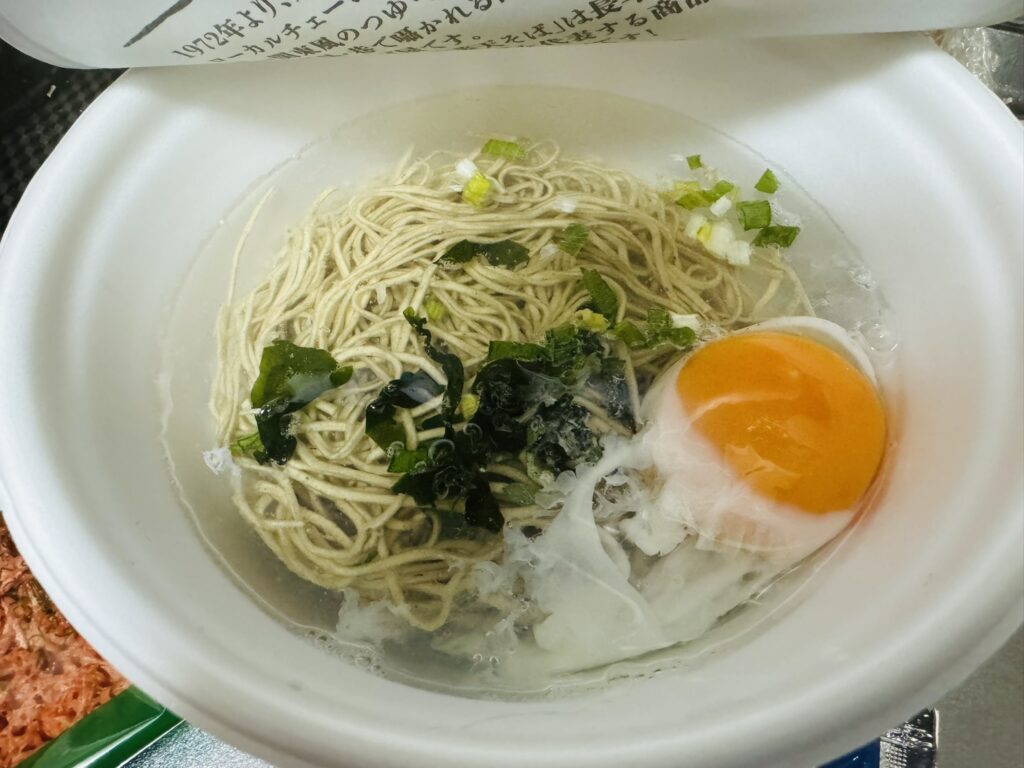 お湯を入れた直後のカップそば。麺の上に卵やわかめ、ねぎのような具材が見えている。