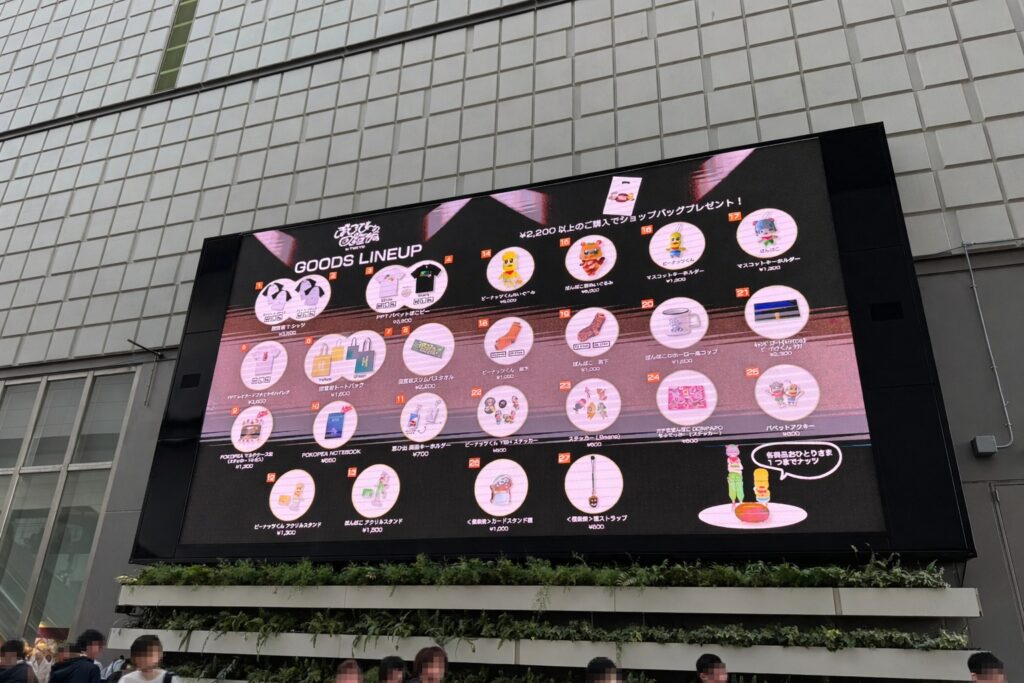 東京ガーデンシアター外の大型ビジョンに『GOODS LINEUP』が表示され、物販の内容が一覧になっている