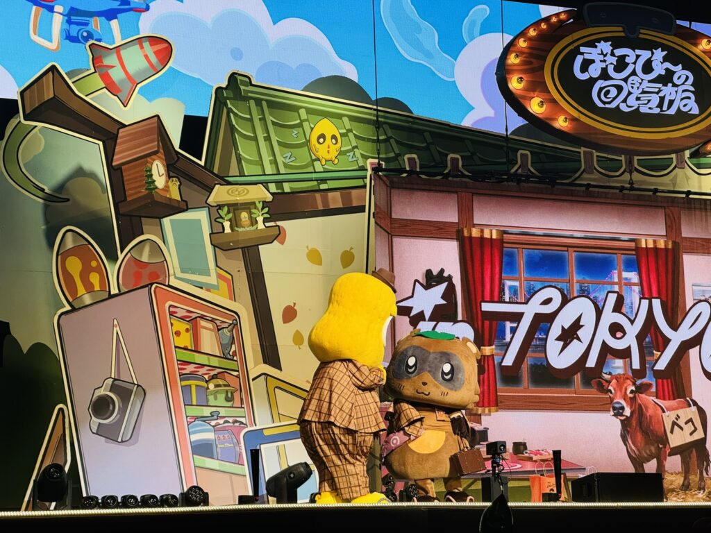 ステージ上のぽこぴーが向き合っているシーン、背景に『TOKYO』の文字が見える